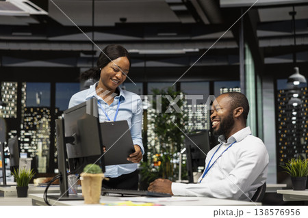 African american staff members consulting each other for monthly reports, reviewing KPI data insights for business productivity late at night. Collaboration between employees for success. African american staff members consulting each other for monthly reports, reviewing KPI data insights for business productivity late at night. Collaboration between employees for success. 138576956