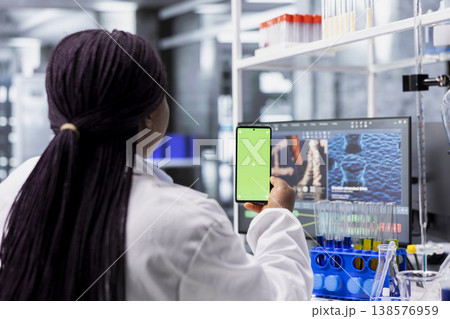 African American female scientist performs research with green screen in laboratory. Using smartphone display and conducting an experiment for biotechnology analysis. Clinical science. 138576959