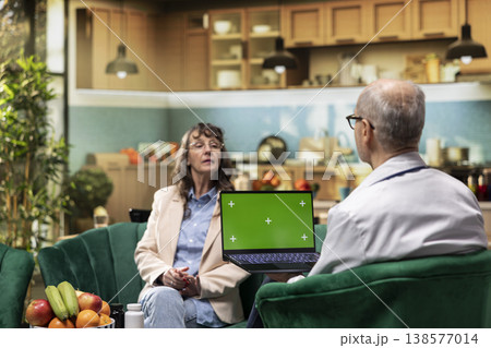 Mockup display on laptop held by senior medic during home care services, conducting healthcare routine exam for old woman. Monitoring vital signs and giving supplements for longevity. 138577014