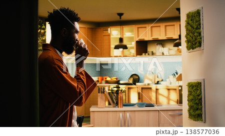 African american man, drinking coffee, relaxing at home, mug in his hands, enjoying natural peace and cozy moment with soft light for a reflective ambience. Person on the weekend, tea time. African american man, drinking coffee, relaxing at home, mug in his hands, enjoying natural peace and cozy moment with soft light for a reflective ambience. Person on the weekend, tea time. 138577036