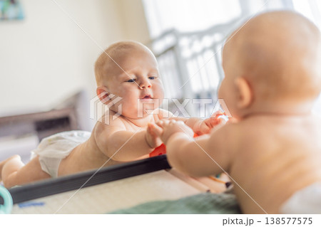 Baby lying on play mat learning to crawl and get on all fours. Infant practicing motor skills and development at home. Early childhood growth, milestones and active learning concept 138577575