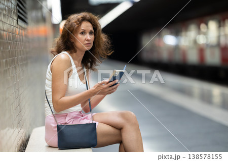 Adult woman sits at subway station with phone 138578155