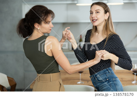 Two joyful middle-aged women dancing together at the kitchen-table with wineglasses 138578170