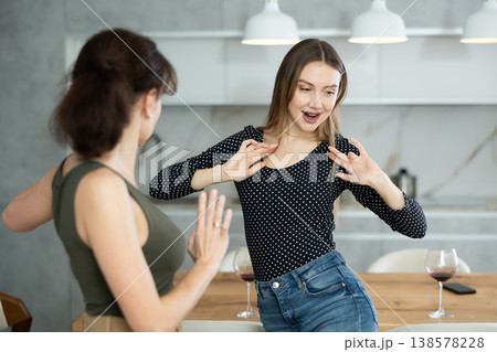 At home two women dance with glass of wine in their hands in kitchen At home two women dance with glass of wine in their hands in kitchen 138578228
