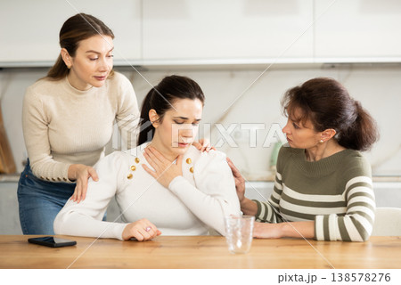 Sad middle-aged woman sitting at table while two others trying to calm her Sad middle-aged woman sitting at table while two others trying to calm her 138578276