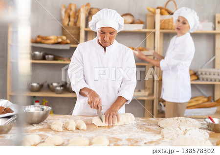 Senior woman baker cutting dough into pieces Senior woman baker cutting dough into pieces 138578302