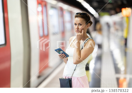 Portrait of gorgeous woman waiting for subway train with smartphone in hands at underground station 138578322