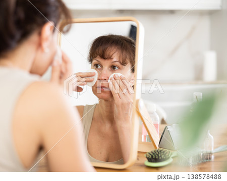 Woman wiping off makeup with cotton pads in front of mirror Woman wiping off makeup with cotton pads in front of mirror 138578488