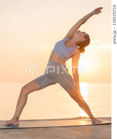 Near sea during sunset, girl performs variations of virabhadrasana 138578718