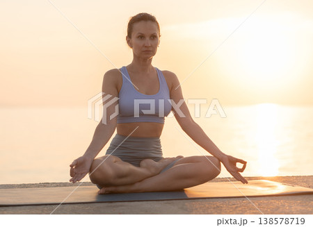 Happy slim woman making yoga meditation in lotus pose on beach at sunrise 138578719