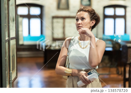 Woman with piece of paper and phone in hands walks around museum hall, view exhibition Woman with piece of paper and phone in hands walks around museum hall, view exhibition 138578720