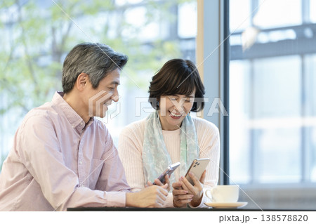 カフェでスマートフォンを見ながら話をする60代の夫婦 カフェでスマートフォンを見ながら話をする60代の夫婦 138578820