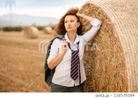 Relaxed businesswoman leaning against haystack during country retreat Relaxed businesswoman leaning against haystack during country retreat 138579394