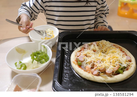 自宅でピザのトッピングを手伝う幼児 自宅でピザのトッピングを手伝う幼児 138581294