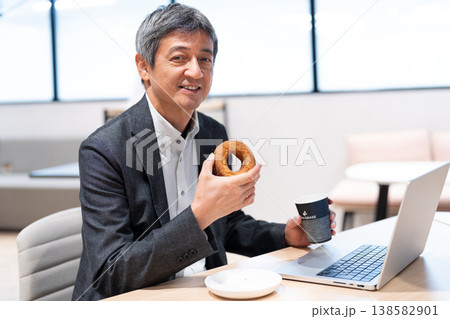 オフィスでドーナツを食べて休憩するミドル層のビジネスマン オフィスでドーナツを食べて休憩するミドル層のビジネスマン 138582901