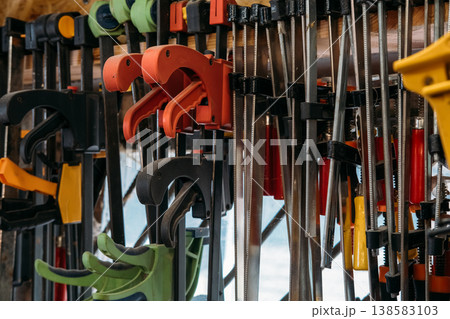 Joinery tools. Bar clamps. Collection of colorful woodworking professional equipment hanging on rack in workshop for joinery projects. Joinery tools. Bar clamps. Collection of colorful woodworking professional equipment hanging on rack in workshop for joinery projects. 138583103
