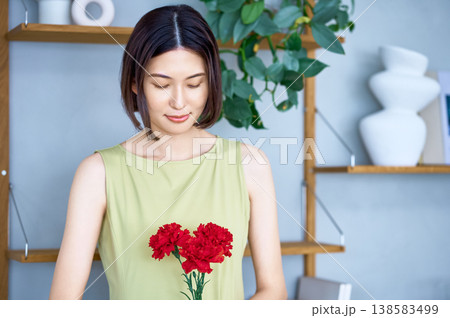 母の日の贈り物に。赤いカーネーションを優しく見つめる若い日本人女性 母の日の贈り物に。赤いカーネーションを優しく見つめる若い日本人女性 138583499