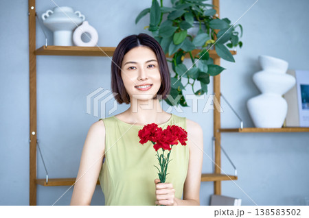 赤いカーネーションを持って微笑む日本人女性。母の日や感謝、お祝いをイメージしたライフスタイル。 赤いカーネーションを持って微笑む日本人女性。母の日や感謝、お祝いをイメージしたライフスタイル。 138583502