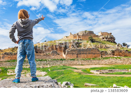 Young child looks at acropolis of ancient Greek city Tlos in Lycia located on Lycian way. Famous historical site In Antalya region. Popular place for family travel on summer vacation. Fethiye, Turkey Young child looks at acropolis of ancient Greek city Tlos in Lycia located on Lycian way. Famous historical site In Antalya region. Popular place for family travel on summer vacation. Fethiye, Turkey 138583609