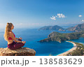 Young woman sit in yoga pose on rock top relaxing, looking at blue lagoon, Oludeniz beach. Summer day walk by Lycian way at family vacation in Mediterranean Sea coast, Fethye, Antalya region, Turkey 138583629