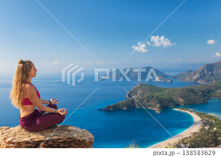 Young woman sit in yoga pose on rock top relaxing, looking at blue lagoon, Oludeniz beach. Summer day walk by Lycian way at family vacation in Mediterranean Sea coast, Fethye, Antalya region, Turkey Young woman sit in yoga pose on rock top relaxing, looking at blue lagoon, Oludeniz beach. Summer day walk by Lycian way at family vacation in Mediterranean Sea coast, Fethye, Antalya region, Turkey 138583629