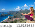 Young woman sit in yoga pose on rock top relaxing, looking at blue lagoon, Oludeniz beach. Summer day walk by Lycian way at family vacation in Mediterranean Sea coast, Fethye, Antalya region, Turkey 138583632