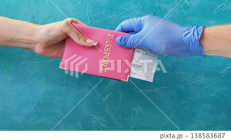 Flight check-in. Quarantine travel. Customs officer hand in protective glove giving pink passport ticket to female passenger on blue. Flight check-in. Quarantine travel. Customs officer hand in protective glove giving pink passport ticket to female passenger on blue. 138583687
