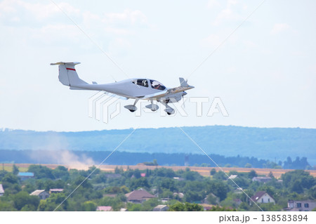Light aircraft flying over green landscape near small houses on a sunny day Light aircraft flying over green landscape near small houses on a sunny day 138583894