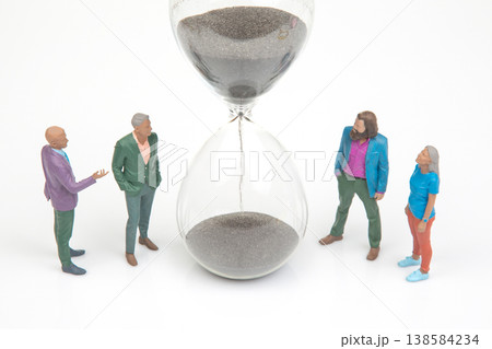 Miniature people gather around an hourglass to discuss time and decisions in a simple setting  138584234