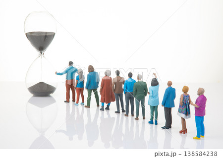 Miniature people stand in line watching an hourglass as sand flows down on a clear background Miniature people stand in line watching an hourglass as sand flows down on a clear background 138584238