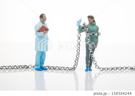 Miniature figures of a doctor and a woman holding a bottle stand near a long chain  138584244