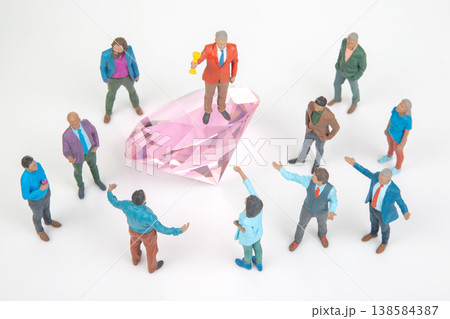 Miniature people gather around a large pink diamond while one holds a trophy and gives a speech 138584387