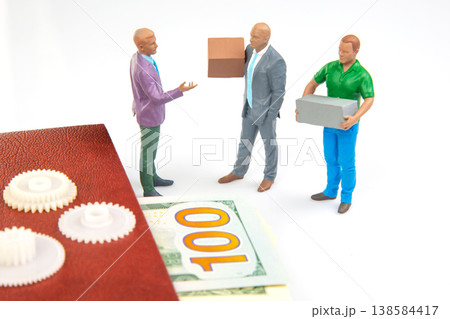 Miniature people discussing business while holding boxes and standing near money on a table Miniature people discussing business while holding boxes and standing near money on a table 138584417