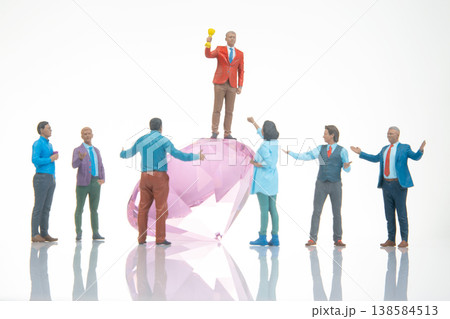 Miniature people celebrate on a large gem while one holds a trophy under bright light Miniature people celebrate on a large gem while one holds a trophy under bright light 138584513