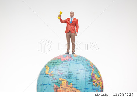 Miniature figurine stands on globe holding trophy showcasing achievement in a bright setting 138584524