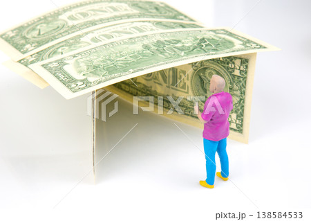 Miniature figurine stands under a dollar bill canopy in a simple setup with focus on the playful Miniature figurine stands under a dollar bill canopy in a simple setup with focus on the playful 138584533