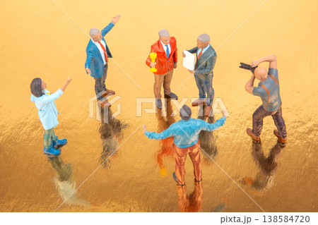 Group of miniature people having a meeting on a shiny surface during the daytime with two figures Group of miniature people having a meeting on a shiny surface during the daytime with two figures 138584720