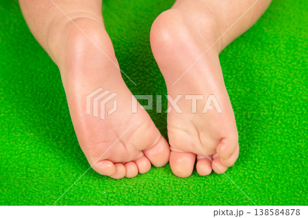 Child's bare feet resting on green surface, showing tiny toes and smooth skin in a playful setting Child's bare feet resting on green surface, showing tiny toes and smooth skin in a playful setting 138584878