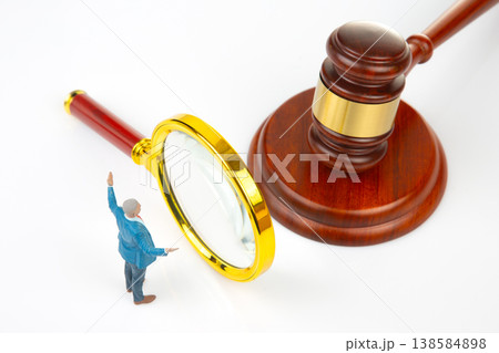 Miniature people using a magnifying glass near a gavel in a legal setting with bright light Miniature people using a magnifying glass near a gavel in a legal setting with bright light 138584898