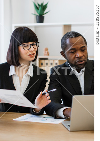 A focused business meeting where colleagues collaborate on documents and a laptop, discussing strategy and data 138585357