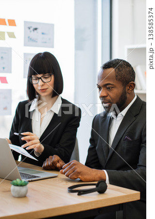 A woman in glasses points at a document while a man listens intently during a business meeting, discussing strategy A woman in glasses points at a document while a man listens intently during a business meeting, discussing strategy 138585374