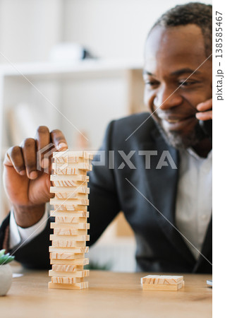 An African American man in a suit plays a game of wooden blocks while talking on the phone, demonstrating focus and multitasking An African American man in a suit plays a game of wooden blocks while talking on the phone, demonstrating focus and multitasking 138585467
