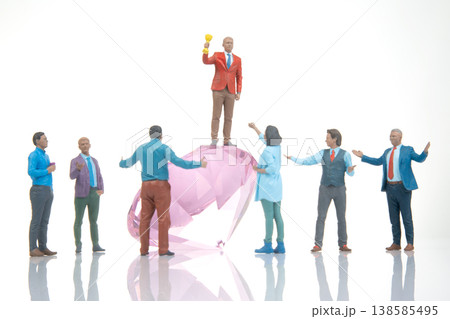 Celebration of success with a group of figures around a large pink gem in an indoor setting 138585495