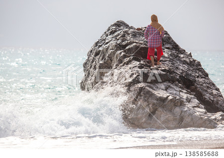 Woman stands on a rock by the sea looking at waves and the horizon in the early morning light  138585688