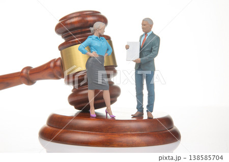 Miniature people stand near gavel and present a document in a lawyer's office setting during daytime Miniature people stand near gavel and present a document in a lawyer's office setting during daytime 138585704