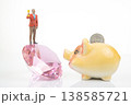 Miniature people stand on a crystal holding a trophy, while a piggy bank waits with a coin resting  138585721