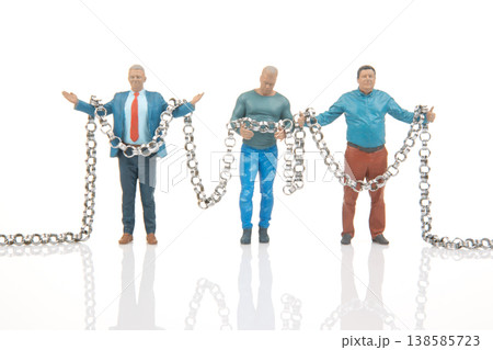 Miniature people hold chains in creative setup showcasing teamwork and cooperation in a unique scene 138585723