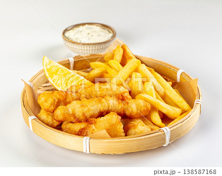 Classic fish and chips served in a basket with lemon and tartar sauce, isolated on white background Classic fish and chips served in a basket with lemon and tartar sauce, isolated on white background 138587168