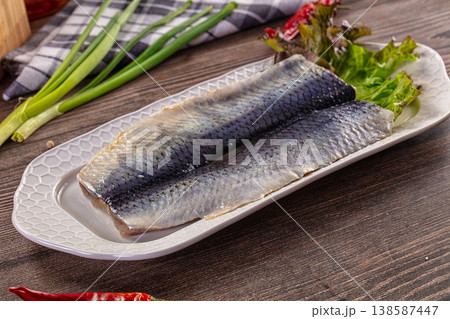 Salted herring fillets served on a white dish with lettuce and green onions 138587447