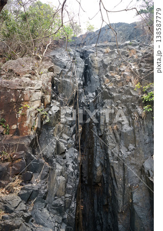 A steep, dark, and rugged rock face in Vietnam with a rope descending, hinting at adventure or a challenging climb A steep, dark, and rugged rock face in Vietnam with a rope descending, hinting at adventure or a challenging climb 138587779